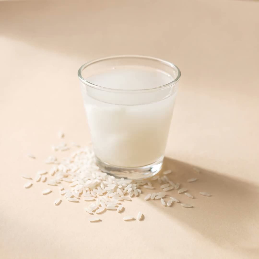 A glass of milky rice water with loose rice grains scattered at its base