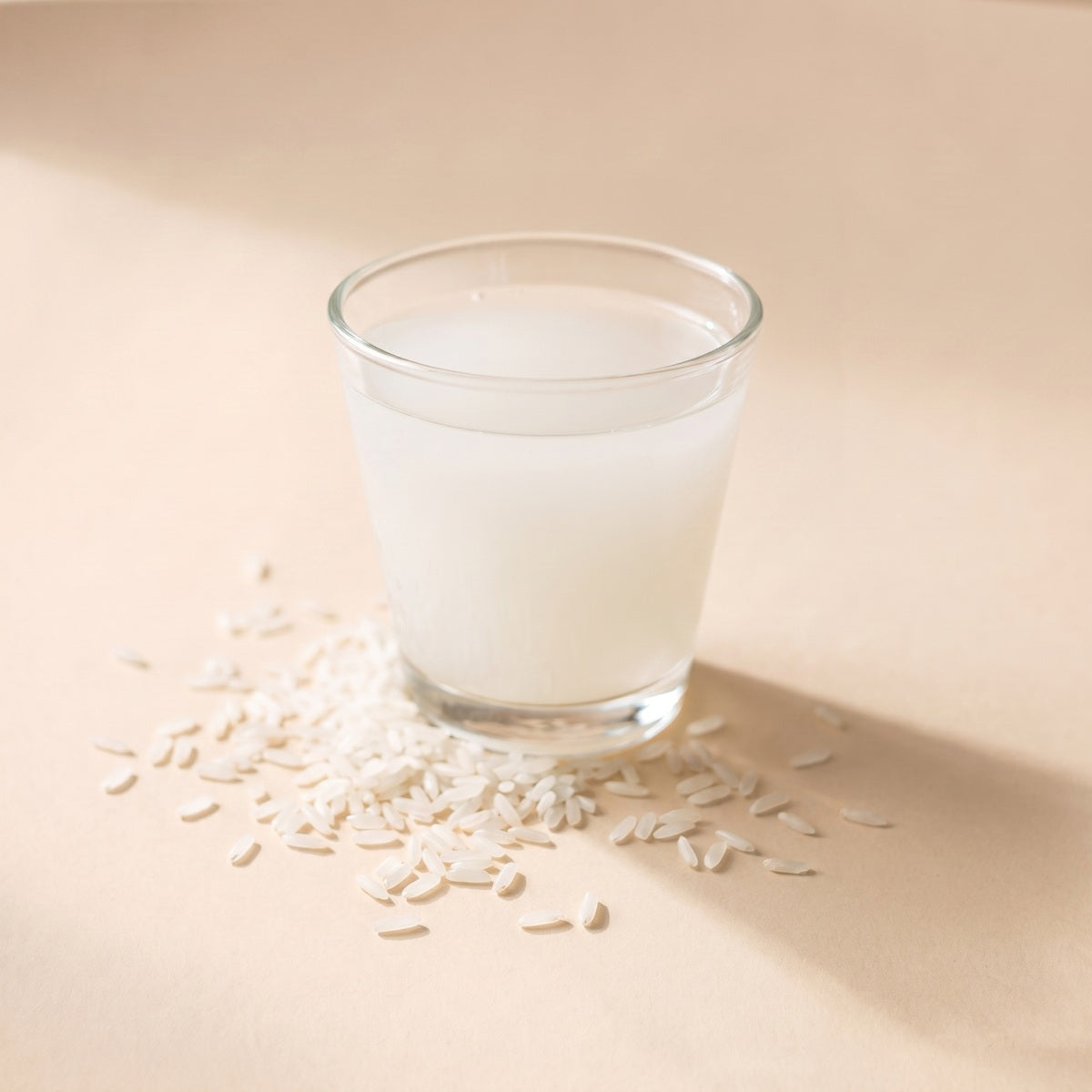 A glass of milky rice water with loose rice grains scattered at its base
